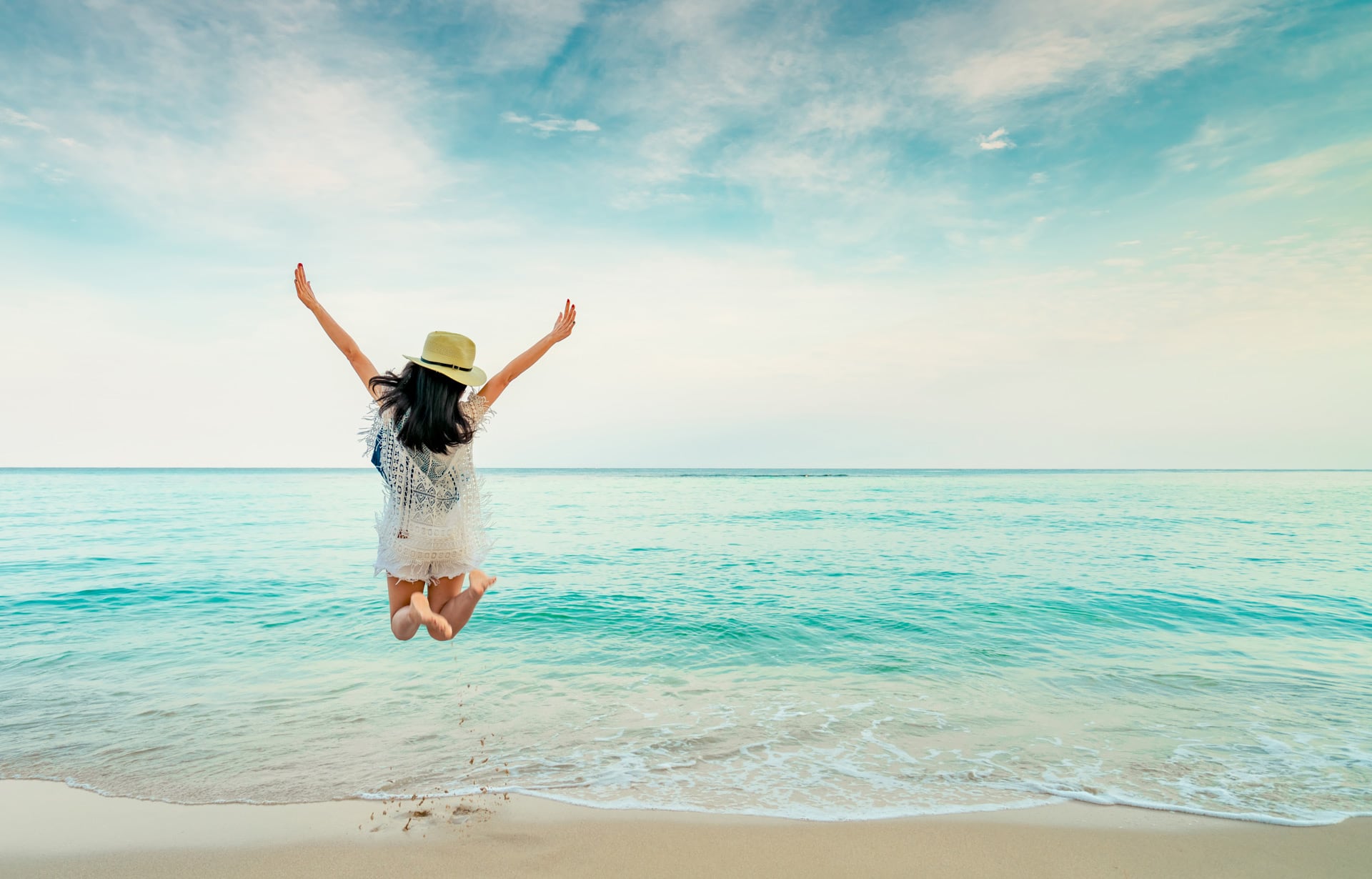 momento Reisen - Frau springt vor Freude am Strand in die Luft