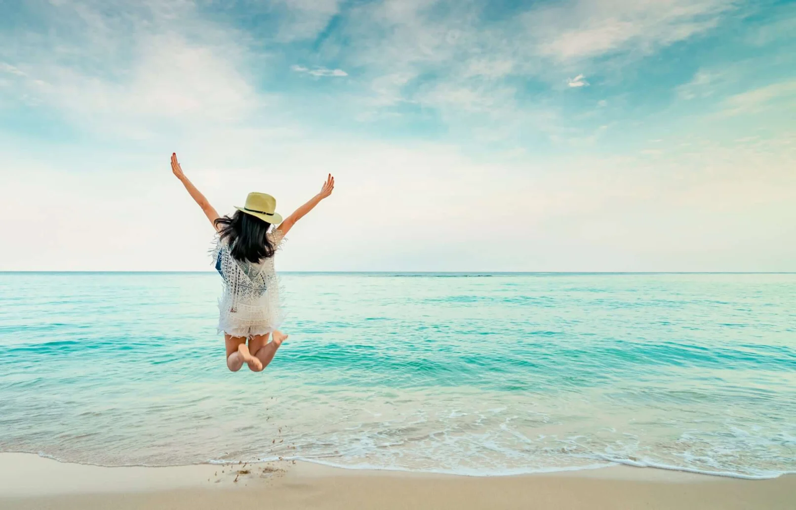 momento Reisen - Frau springt vor Freude am Strand in die Luft